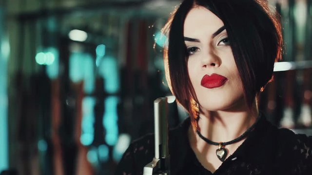 Portrait of a dark-haired girl with red lips and a gun in the hands of.