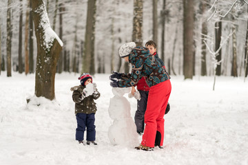 Fototapeta na wymiar Mother and two sons play and molded from snow snowmen in the win