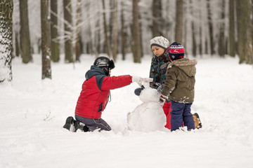 Mother and two sons play and molded from snow snowmen in the win