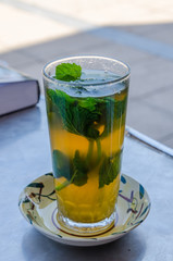Traditional sweet Moroccan tea with mint leaves in tall glass on outside table, Morocco, North Africa