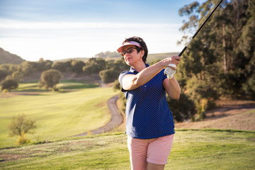 Mature woman playing golf. Golfer hitting golf shot with driver club on course. Beautiful sunny Landscape, green hills, blue sky. Portugal. 