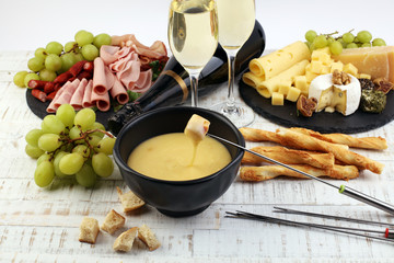 Gourmet Swiss fondue dinner on a winter evening with assorted cheeses on a board alongside a heated...