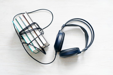 Books and headphones on wooden white surface. Concept of listening to audiobooks.