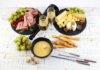 Gourmet Swiss fondue dinner on a winter evening with assorted cheeses on a board alongside a heated...