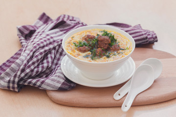 Суп с фрикадельками и лапшой в белой миске на деревянном фоне