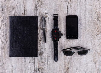 black men's items on a wooden table, a watch, a notebook, glasses, fountain pen and cell phone, businessman