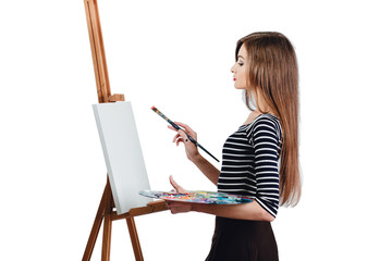 Cute beautiful girl artist painting a picture on  canvas  easel. Space for text. Studio white background, isolated.