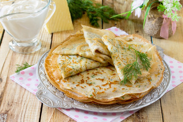 Not sweet pancakes with cheese and fresh dill on a wooden table.