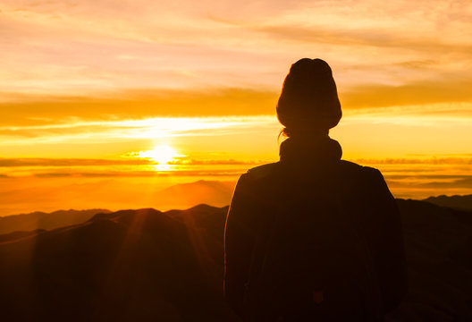Female hiker watching the sunrise from a mountain top. 