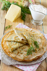 Not sweet pancakes with cheese and fresh dill on a wooden table.