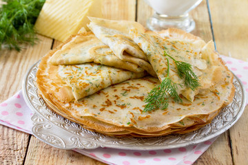 Not sweet pancakes with cheese and fresh dill on a wooden table.