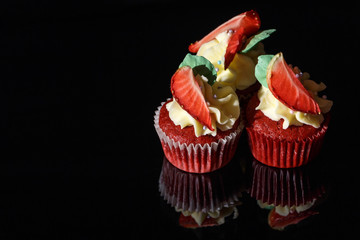Red velvet cupcakes with strawberries on black glass.