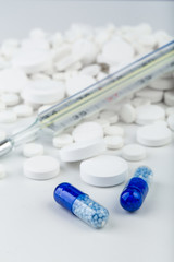 Bunch of white tablets with blue pills and thermometer.