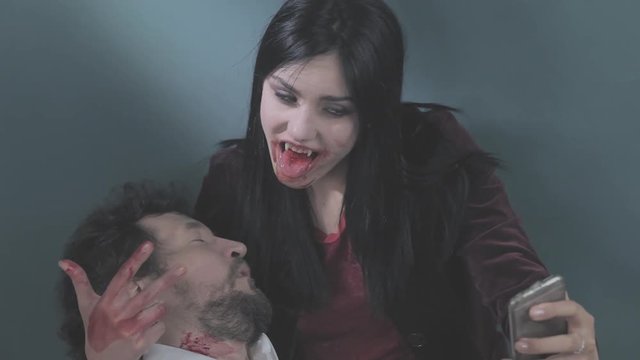 Funny female vampire taking selfie with cell phone holding dead man/Vampire taking picture with cell phone