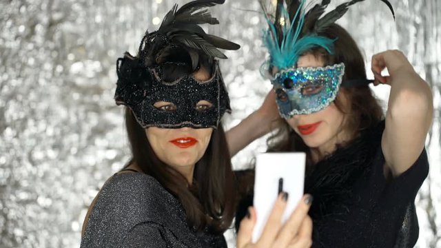 Beautiful women in carnival masks doing photo on smartphone, steadycam shot
