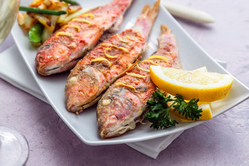 Plate of fried small fish red mullet and lemon, close view