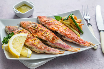 Plate of fried small fish red mullet and lemon, close view
