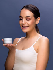 Smiling pretty woman holding cosmetic cream for her skin.