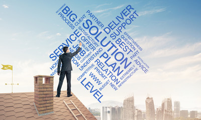 Young businessman standing on house roof and writing leadership 