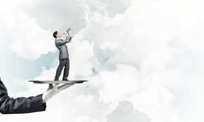 Businessman on metal tray playing fife against blue sky background