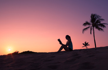 Young woman reading book on the beach. 