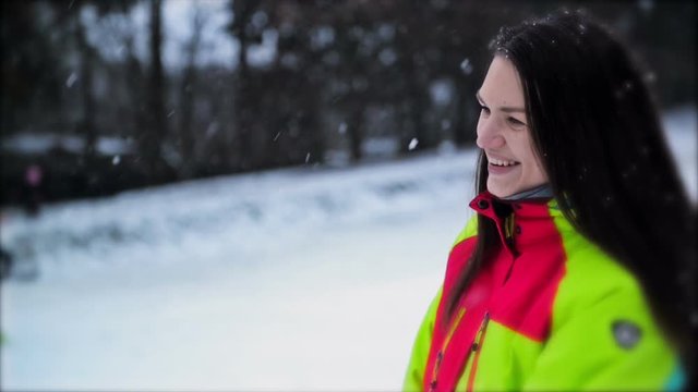 Closeup Portrait of Woman Wearing Colorful Ski Suit, Snowflakes Slowly Falling Down. Cute Young Girl with Long Hair and Wonderful Smile Enjoying Winter Outdoors.