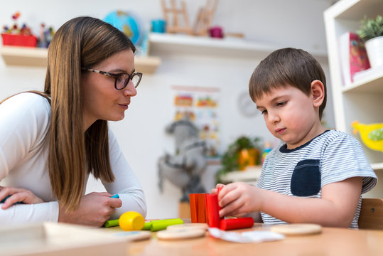 Woman looking at kid playing with didactic colorful toys indoors - preschool