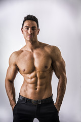 Fototapeta premium Handsome shirtless muscular man with elegant pants, standing, on light background