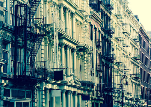 Fototapeta New York City view of exterior facade on ornate old apartment building residence with fire escapes seen from lower Manhattan with vintage retro filter effect. 
