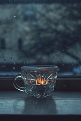 Candle in crystal cup lit in rainy day window