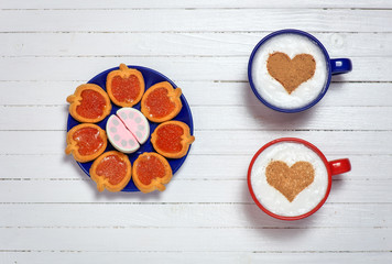 Two cups of coffee with heart shape symbol and sweets on wooden
