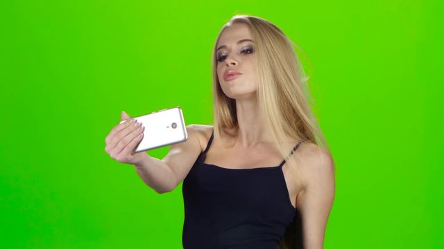 On the smartphone camera blonde girl doing selfie. Green screen