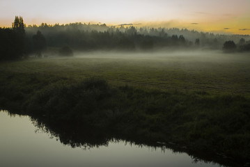 Sunrise on the field with fog near the river bank