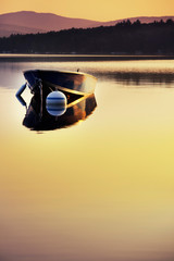 Small boat moored at a buoy in calm Merrymeeting Lake bathed in sunrise light