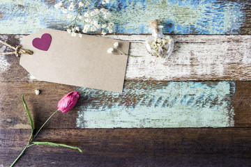Love concept of blank brown paper tag with red heart and flowers on old wood for valentines day and wedding