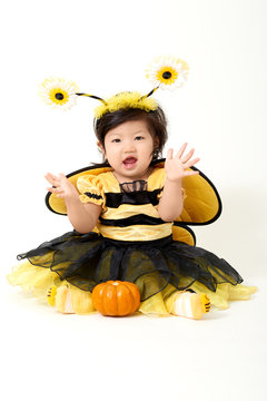 Baby girl dressed as cute little bee with a small pumpkin smiling