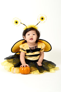 Baby girl dressed as cute little bee with a small pumpkin smiling