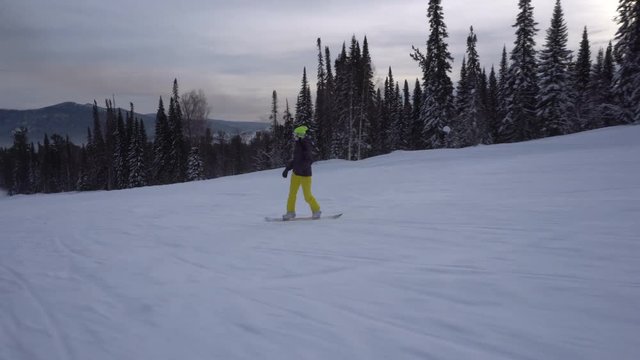 Woman is drifting fast on a snowboard from snow-covered mountains slope at cloudy day