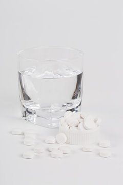 Round white pills and glass of water on a table.