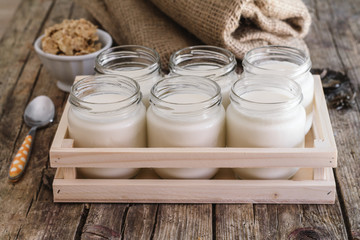 Homemade yogurt in glass jar and wooden box. Antique wooden table. Burlap and cereal bowl on background. Steel teaspoon orange and white dots