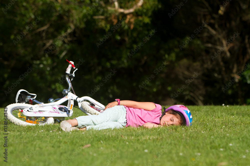 Wall mural young caucasian child girl sleeping near her bike on natural bac