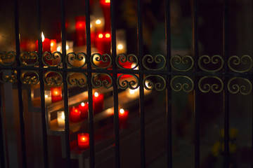 Candle light behind the iron fence. Lots of candles lit up.