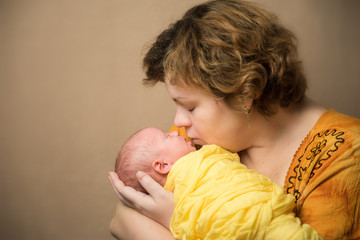 Mother kissing newborn baby. Yellow colored clothes
