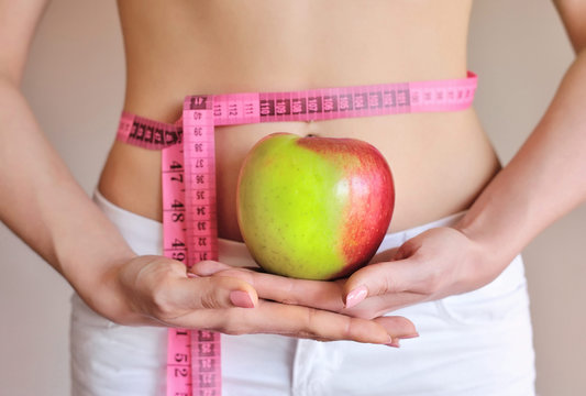 Woman measuring her waist while holding an apple