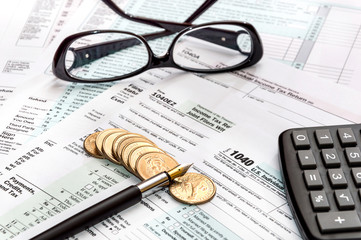 Pen, glasses, calculator and coins on tax forms. Business concep