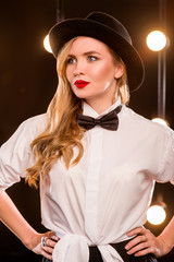 young blonde attractive woman in white shirt, butterfly, black hat with microphone singing on stage