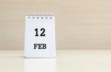 Closeup surface note book with black 12 feb word in page on blurred brown wood desk and wood wall textured background with copy space under window light