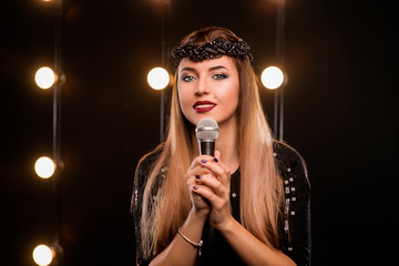 young smiley beautiful long hair girl in black dress with microphone singing song on the stage in karaoke