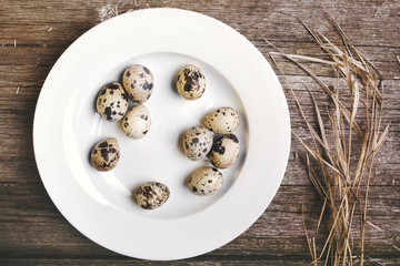 quail eggs on old wooden table, rustic background with straw