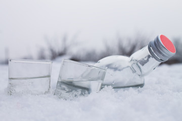 Bottle with glasses of vodka lying on ice